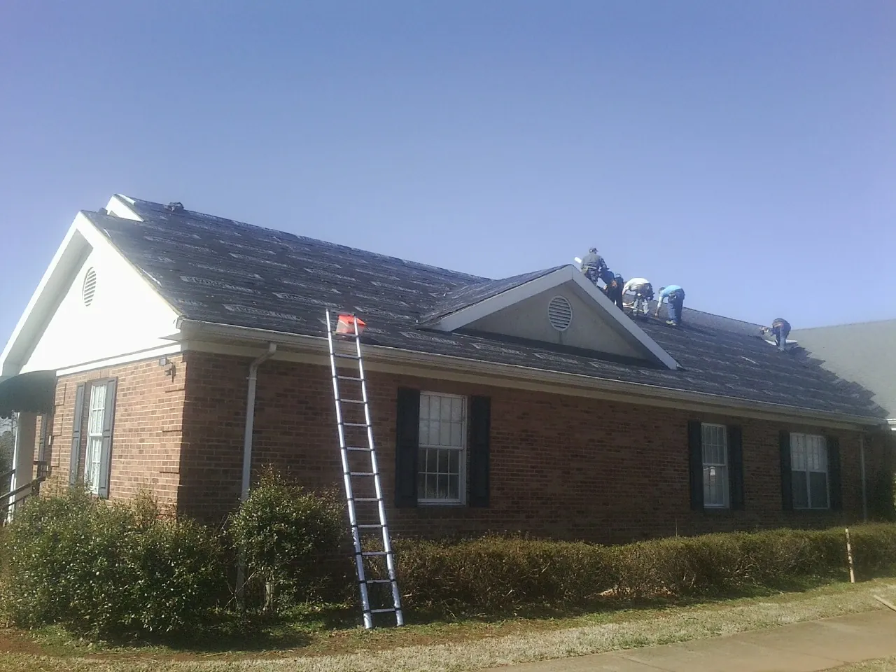 Crew tearing shingles off a brick ranch roof with a ladder set — Metal Roof Repair work by our crew in Dennis
