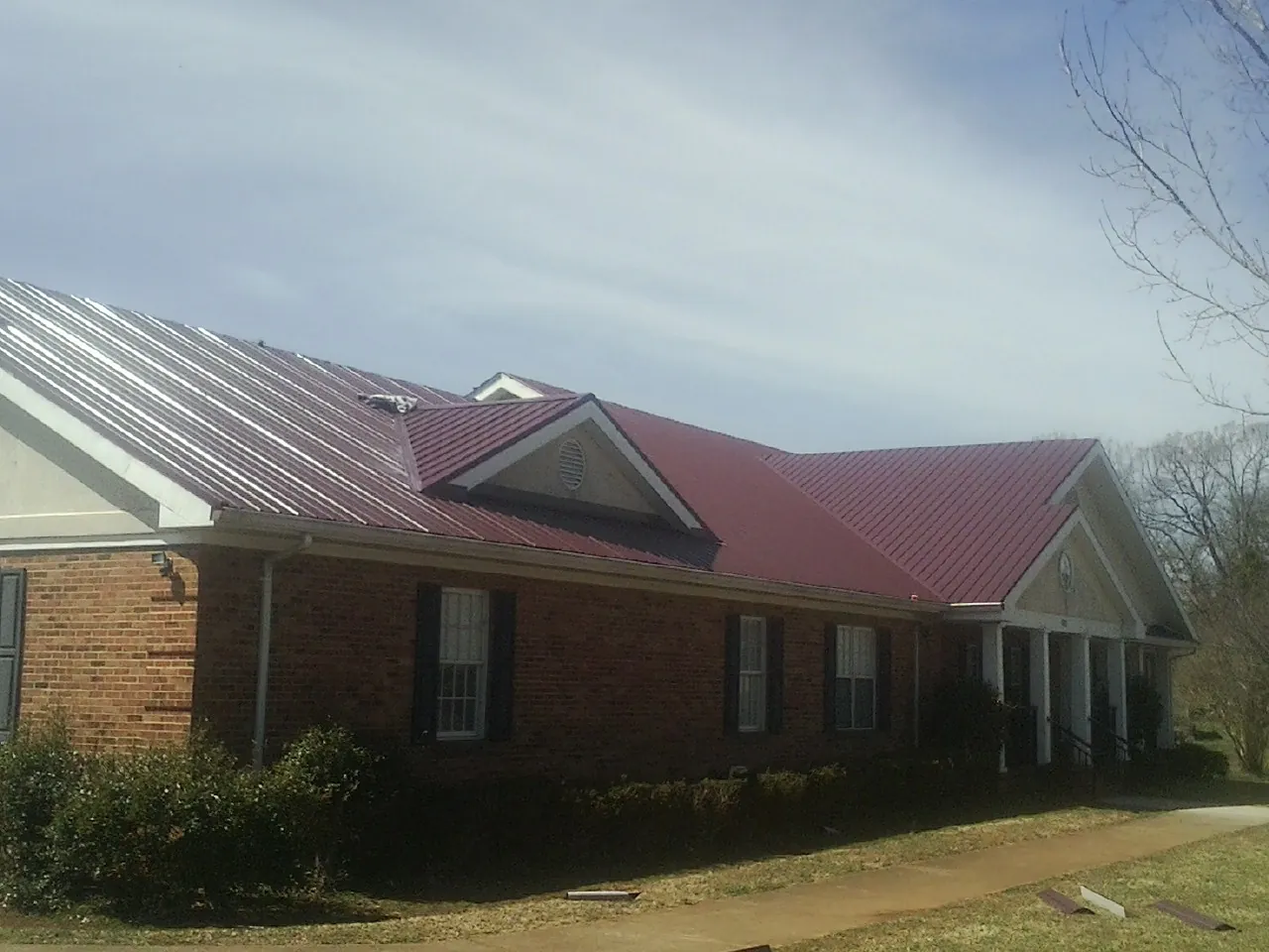 Red metal roof with gabled entries on a long brick building, from a Hail Damage Roof Repair job in Dennis
